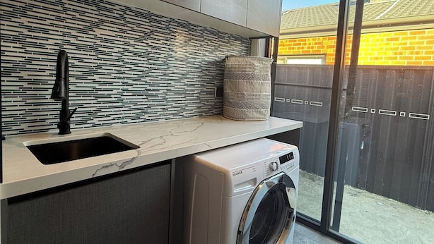 A compact kitchen with a built-in washing machine, a sink, and a tiled backsplash. - Bright Kalkallo Home, Easy Melbourne Access (Kalkallo)