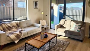 A living room with two sofas, a coffee table, and a view through a sliding glass door. - Bright Kalkallo Home, Easy Melbourne Access (Kalkallo)