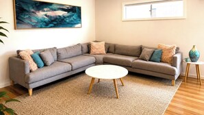Ein Wohnzimmer mit einem grauen Ecksofa, einem runden Couchtisch und einem großen abstrakten Gemälde an der Wand.