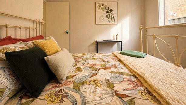 Ein Schlafzimmer mit einem Bett, einem Nachttisch, einem gerahmten Kunstwerk an der Wand und einem Fenster.