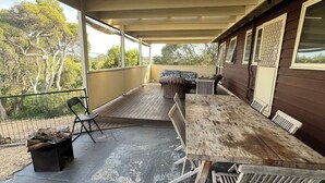 An outdoor covered patio with a wooden table and chairs, a cushioned bench, and a fire pit. - Retro Beach Shack in the Heart of Rye (Rye)