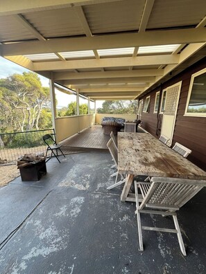 An outdoor covered patio with a wooden table and chairs, a cushioned bench, and a fire pit. - Retro Beach Shack in the Heart of Rye (Rye)