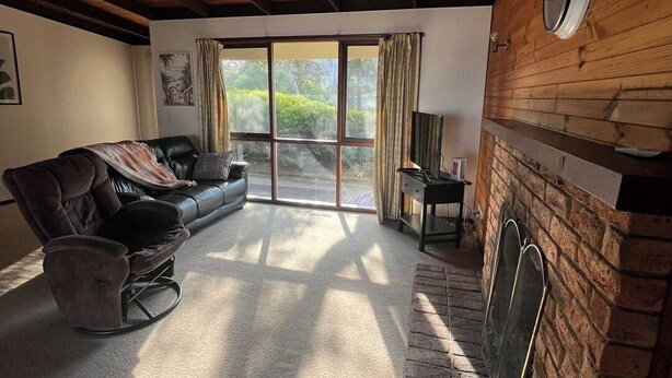 A spacious living room with a fireplace, a sofa, a rocking chair, and a large sliding glass door leading to a deck. - Retro Beach Shack in the Heart of Rye (Rye)