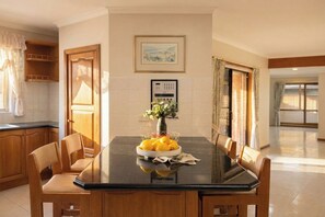 A dining area with a black table, wooden chairs, a vase with flowers, and a bowl of fruit. - 4BR Home Near Altona Beach · Sleeps 9 · Yard (Altona Meadows)