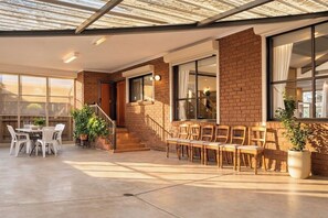 A spacious patio area with a concrete floor, a brick exterior, and a covered seating area with chairs and a table. - 4BR Home Near Altona Beach · Sleeps 9 · Yard (Altona Meadows)