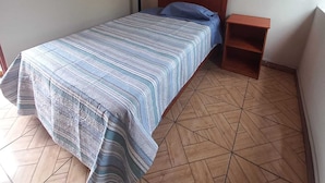 A single bed with a striped bedspread, a wooden headboard, a nightstand, and a coat rack against a plain wall. - ILLA HOSTELS (Arequipa)