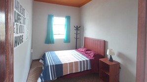 A bedroom with a bed, a nightstand, a lamp, a window with curtains, and a wall with a motivational quote. - ILLA HOSTELS (Arequipa)