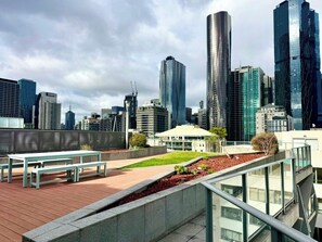 A cityscape with modern high-rise buildings, a rooftop garden with benches, and a glass railing overlooking the city. - Compact Stay with Balcony, Rooftop and Gym (West Melbourne)