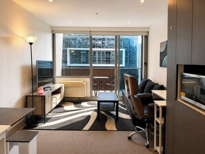 A modern hotel room with a sofa, a desk, a chair, a television, and a large window offering a city view. - Compact Stay with Balcony, Rooftop and Gym (West Melbourne)