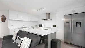A modern kitchen with white cabinetry, a stainless steel refrigerator, and a central island. - Location, Location...This seaside unit has it all (Surfers Paradise)