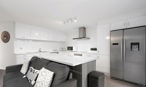 A modern kitchen with white cabinetry, a stainless steel refrigerator, and a central island. - Location, Location...This seaside unit has it all (Surfers Paradise)