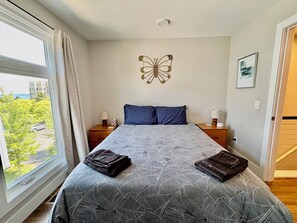 A bedroom with a large bed, two nightstands, a wall-mounted butterfly decoration, and a window with curtains. - The Nest, TC Downtown + Beach, Rooftop + Garage (Traverse City)