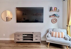 A living room with a flat-screen TV, a round mirror, a grey sofa, a wooden TV stand, and two bookshelves. - The Nest, TC Downtown + Beach, Rooftop + Garage (Traverse City)