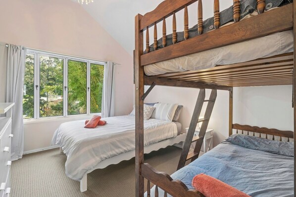 A bedroom with bunk beds, a window with curtains, and a view of greenery outside.