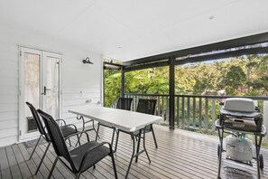 A covered outdoor area with a table and chairs, a grill, and a view of greenery.