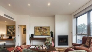 A modern living room with a fireplace, large windows, and artwork on the walls. - Bright and Spacious Penthouse by Parliament House (Forrest)