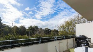A balcony with a metal railing, a table with a helmet and a bottle, and a view of trees and a building in the background. - Bright and Spacious Penthouse by Parliament House (Forrest)