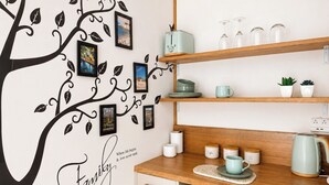 Cocina con un adhesivo de pared de un árbol y fotografías, estantes de madera con cristalería y plantas, y una cafetera.