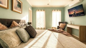 Un dormitorio con una cama, una silla, un escritorio y un televisor en la pared.