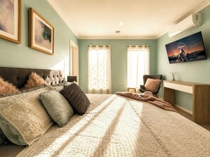 Un dormitorio con una cama, una silla, un escritorio y un televisor en la pared.