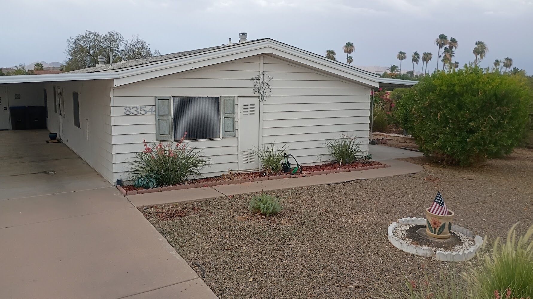 A single-story house with a garage, a small front yard with a gravel path, and a decorative American flag.