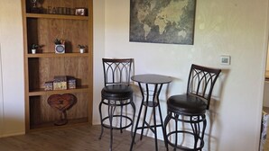 Una habitación con una estantería de madera, dos sillas negras, una pequeña mesa redonda y un mapa del mundo en la pared.