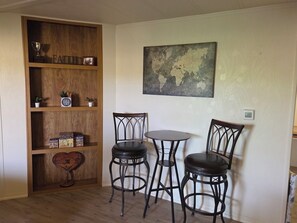 A room with a wooden bookshelf, two black chairs, a small round table, and a world map on the wall. - Charming 55+ Arizona Getaway (Mesa)