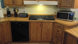 Una cocina con armarios de madera, lavavajillas negro, estufa y microondas.