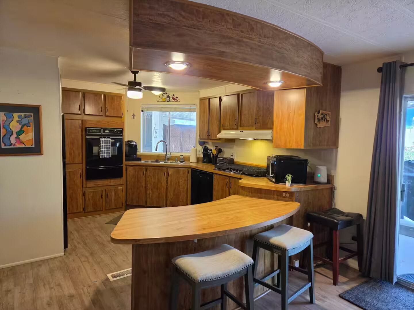 A kitchen with wooden cabinets, a built-in oven, a microwave, and a bar area with stools.