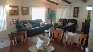 A living room with a dark leather sofa, a wooden dining table with chairs, and a coffee table. - Charming 55+ Arizona Getaway (Mesa)