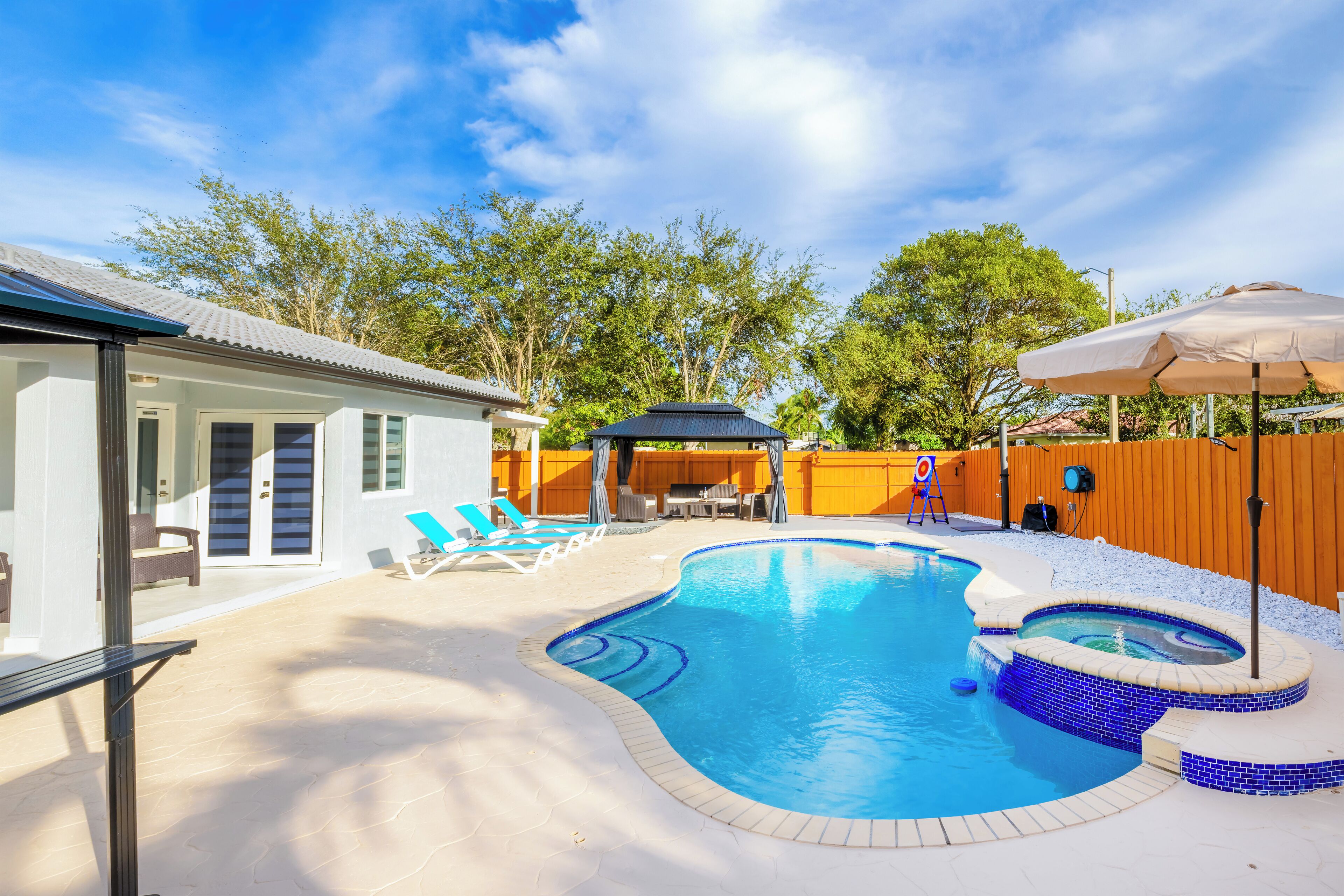 A backyard with a swimming pool, lounge chairs, and a hot tub.