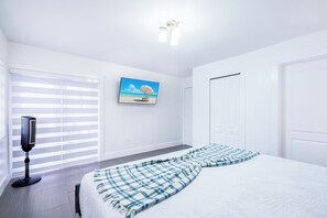 A bedroom with a bed, a television, a painting, and a window with blinds. - Miami Relax  Heated Pool  Family Getaway (Princeton)