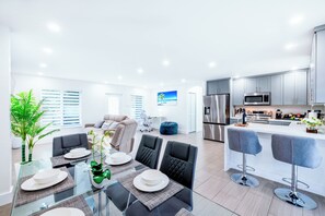 A modern kitchen with stainless steel appliances, a dining area with a glass table and chairs, and a living space with a sofa and a coffee table. - Miami Relax Heated Pool Family Getaway (Princeton)