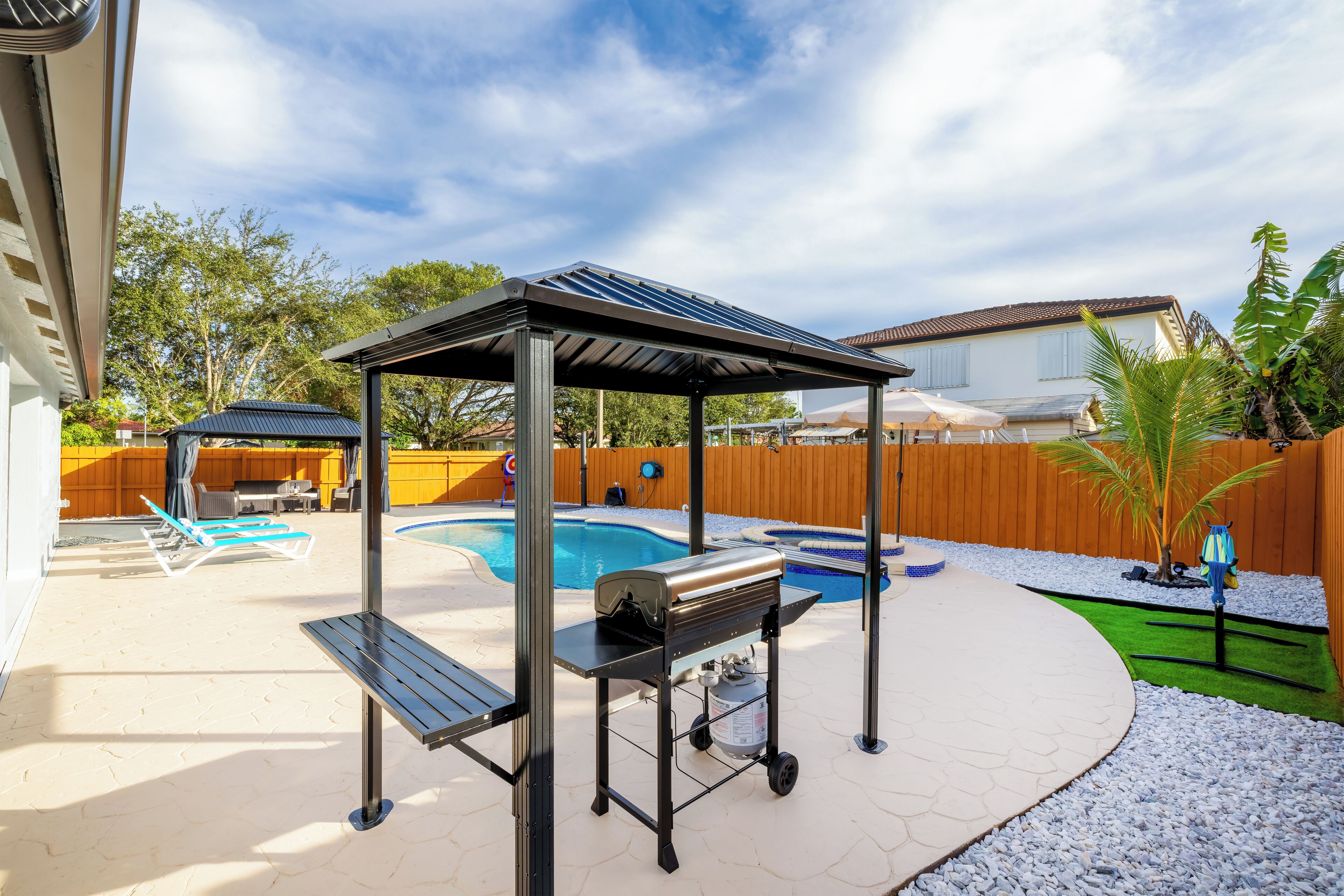 Ein Garten mit Pool, Grillplatz und überdachter Sitzgelegenheit.
