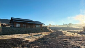 Un edificio in legno con tetto spiovente, un'area recintata e un sentiero sterrato che si allontana.