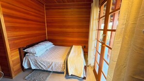 A wooden room with a bed, a window with curtains, and a door.