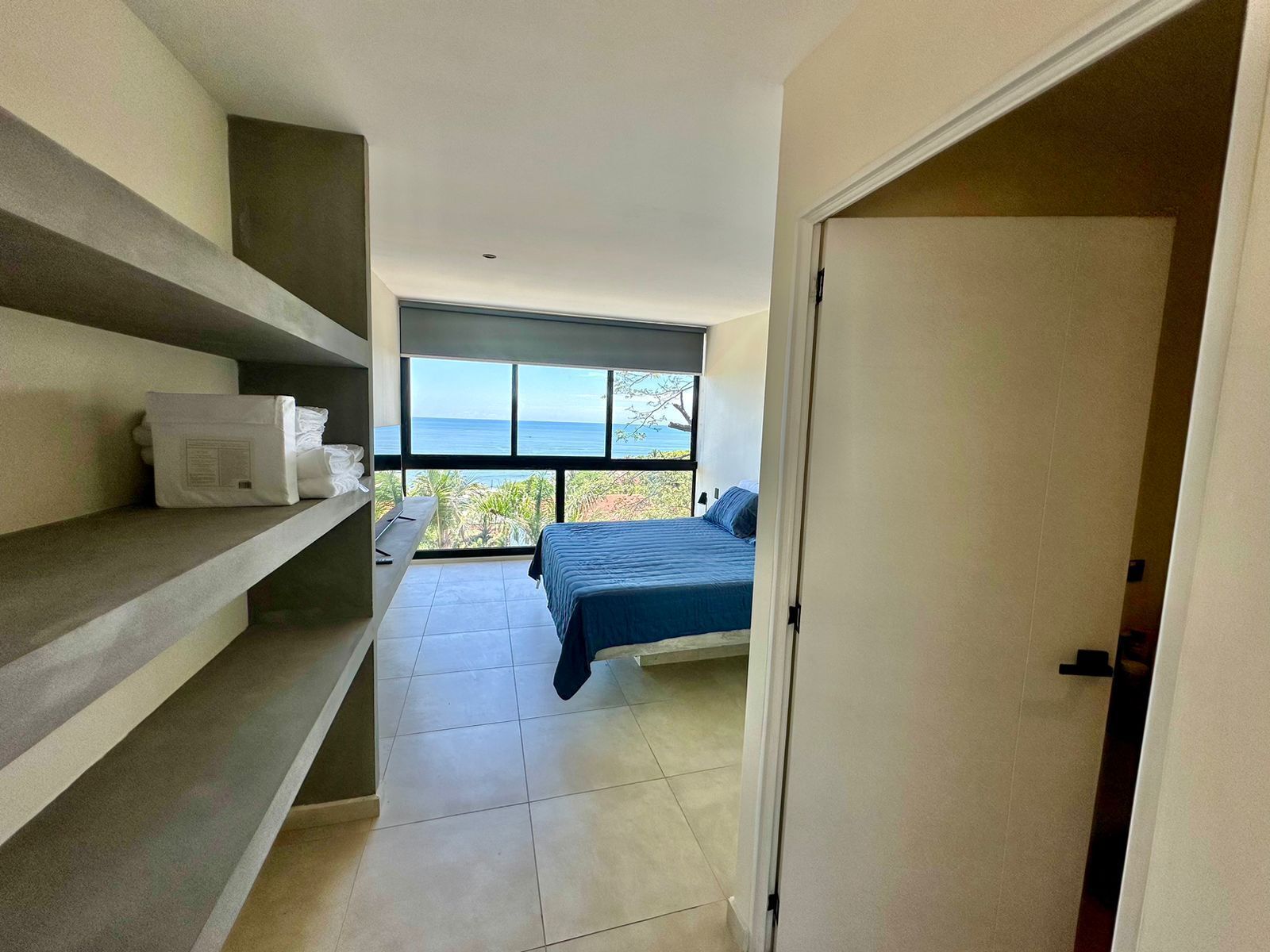Un dormitorio con cama, ventana con vistas al mar y estante con toallas.