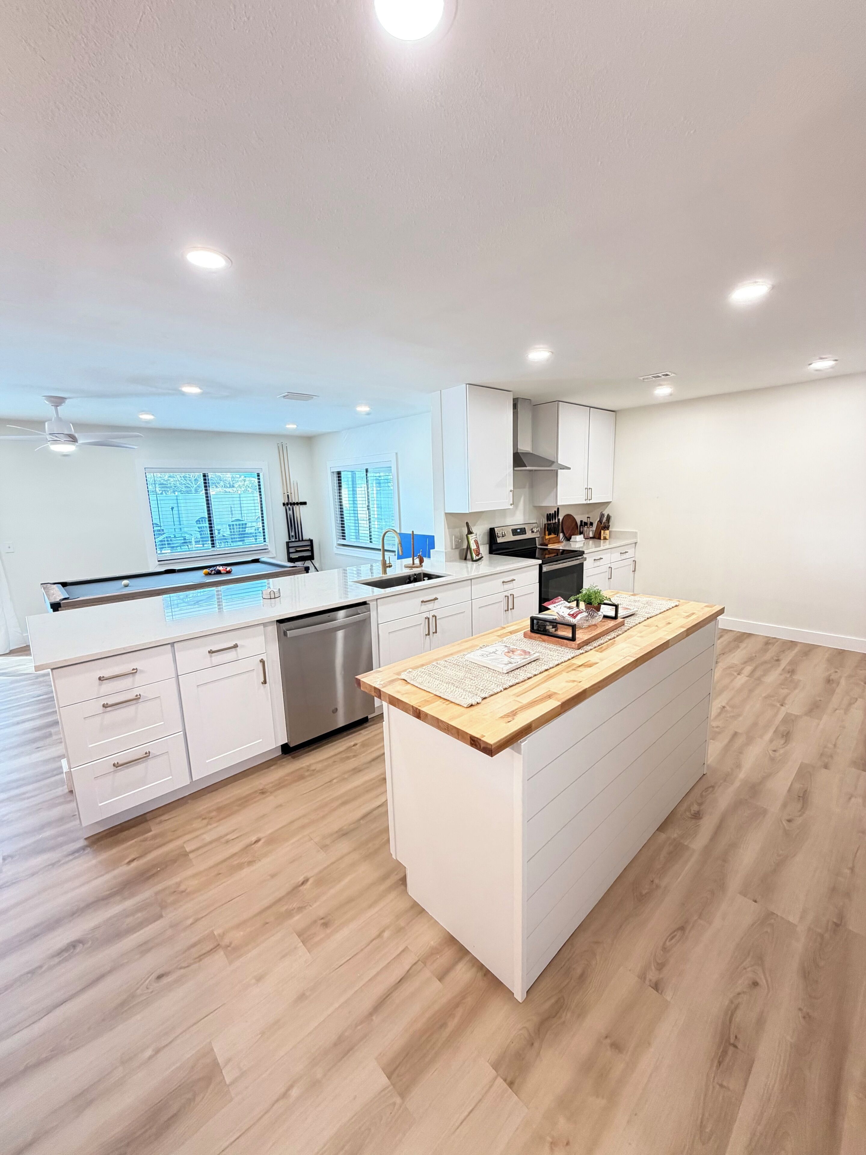 Una cucina moderna con mobili bianchi, un'isola con piano in legno e una lavastoviglie.