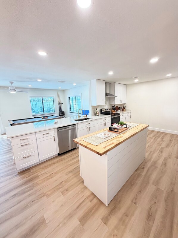 Une cuisine moderne avec des meubles blancs, un îlot central doté d’un plan de travail en bois et un lave-vaisselle.
