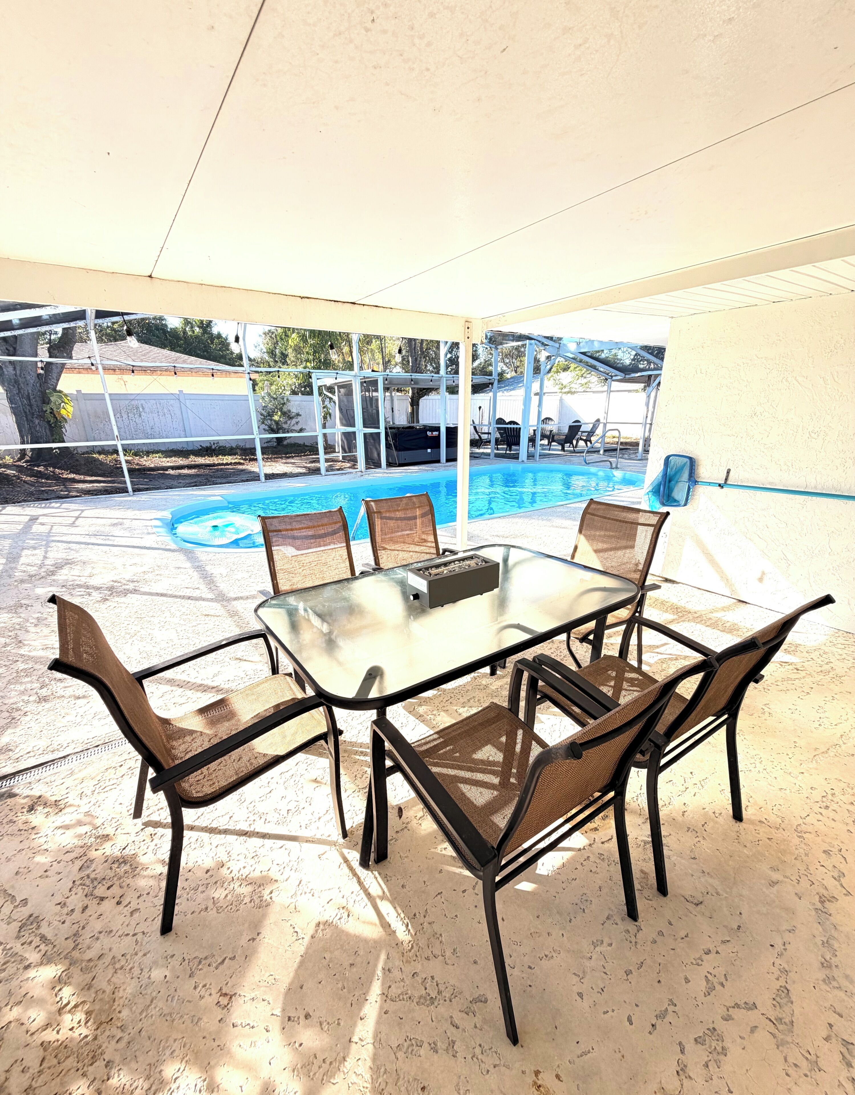 An outdoor patio with a glass table and chairs, a pool, and a covered area.