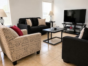 A living room with a black sofa, a patterned armchair, a coffee table, and a TV on a stand. - Luxury 5BR Orlando Villa | Private Pool & Spa | Games Room | Near Disney (Davenport)
