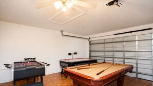 Um quarto com mesa de pebolim, mesa de bilhar e ventilador de teto.