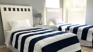 Quarto com duas camas, cada uma com cabeceira branca e edredom listrado em azul marinho e branco.