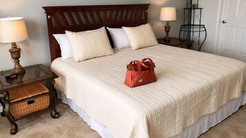 Una cama bien hecha con cabecera de madera, dos mesitas de noche con lámparas, una cesta de mimbre y un bolso rojo sobre la cama.