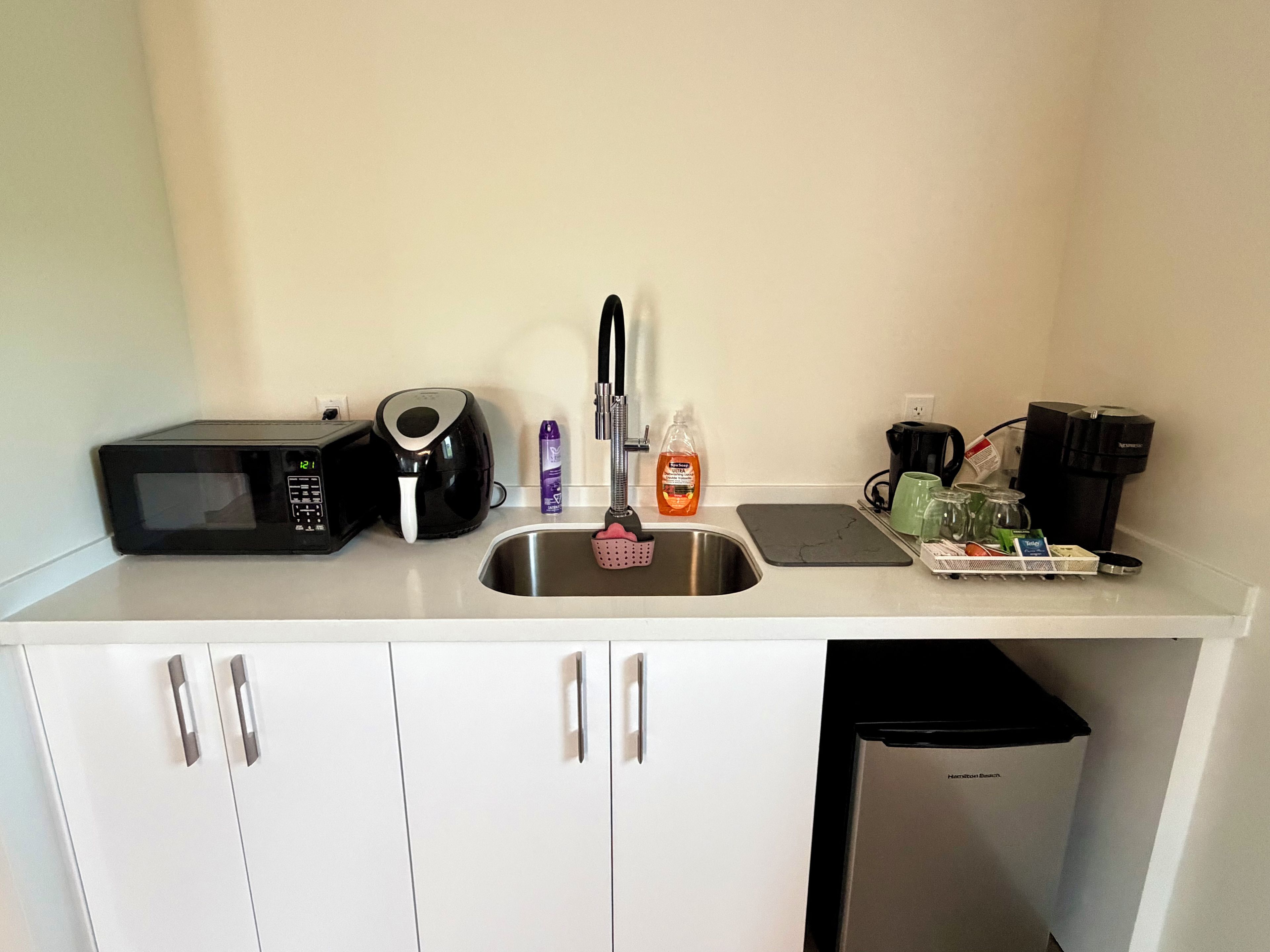 Cozinha compacta equipada com micro-ondas, cafeteira e pia com frasco de detergente.