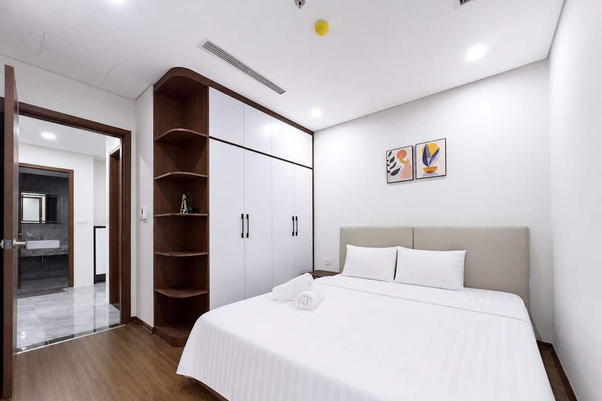 Quarto moderno com cama, guarda-roupa e banheiro visível por uma porta aberta.