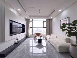 A modern living room with a flat-screen TV, a sofa, a coffee table, and a large window with a city view. - The Elite Premier Suites (Hanoi)