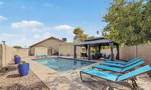 Ein Pool mit Liegestühlen und einer überdachten Sitzgelegenheit.
