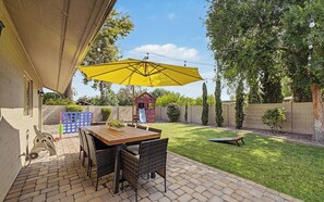 Eine Terrasse mit Tisch und Stühlen, einem gelben Sonnenschirm und einer Spielanlage für Kinder.