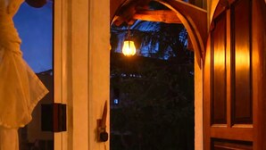 Een houten deur met een ruit, een rode balustrade en een hangende lamp.